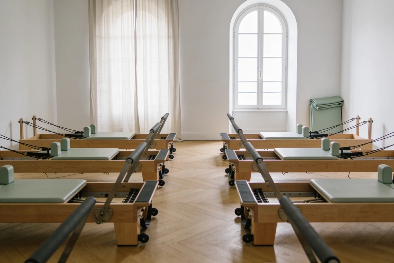 La salle vide : huit Reformers alignés sur le parquet de chêne, grande fenêtre