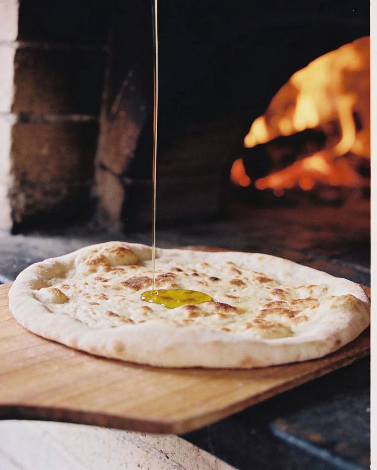 Pain plat sorti du four à bois et filet d’huile d’olive sur une planche en bois